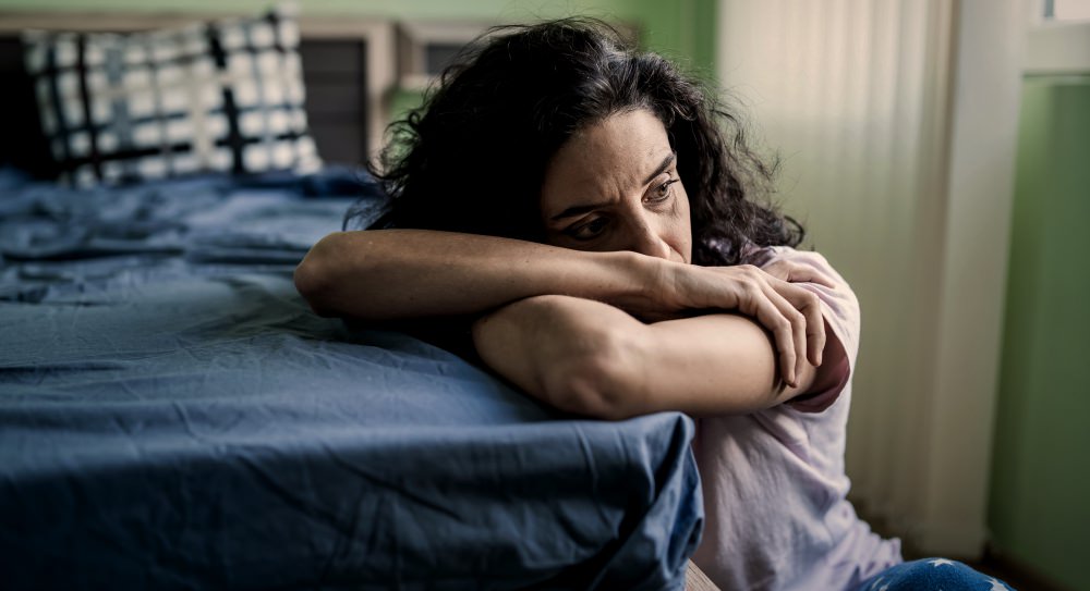 Worried Woman Sitting On Floor Next To Bed