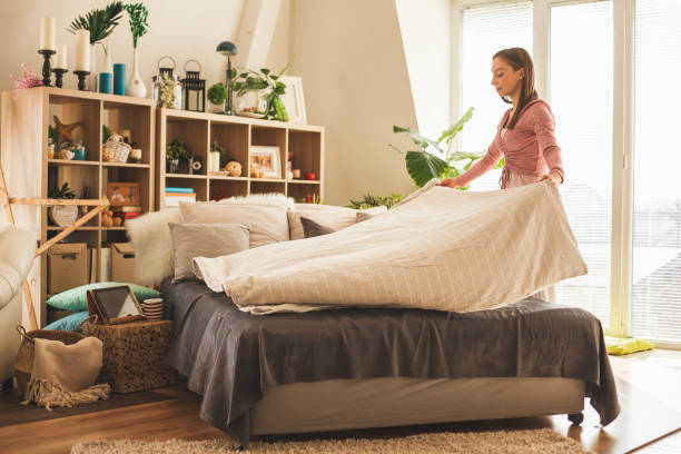 Young Woman Making Bed In Her Bedroom In The Morning.