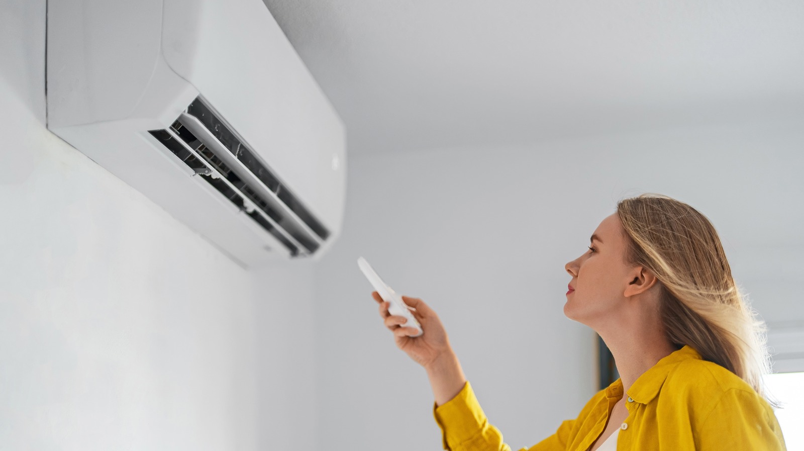 Woman,Holding,Remote,Control,Aimed,At,The,Air,Conditioner.
