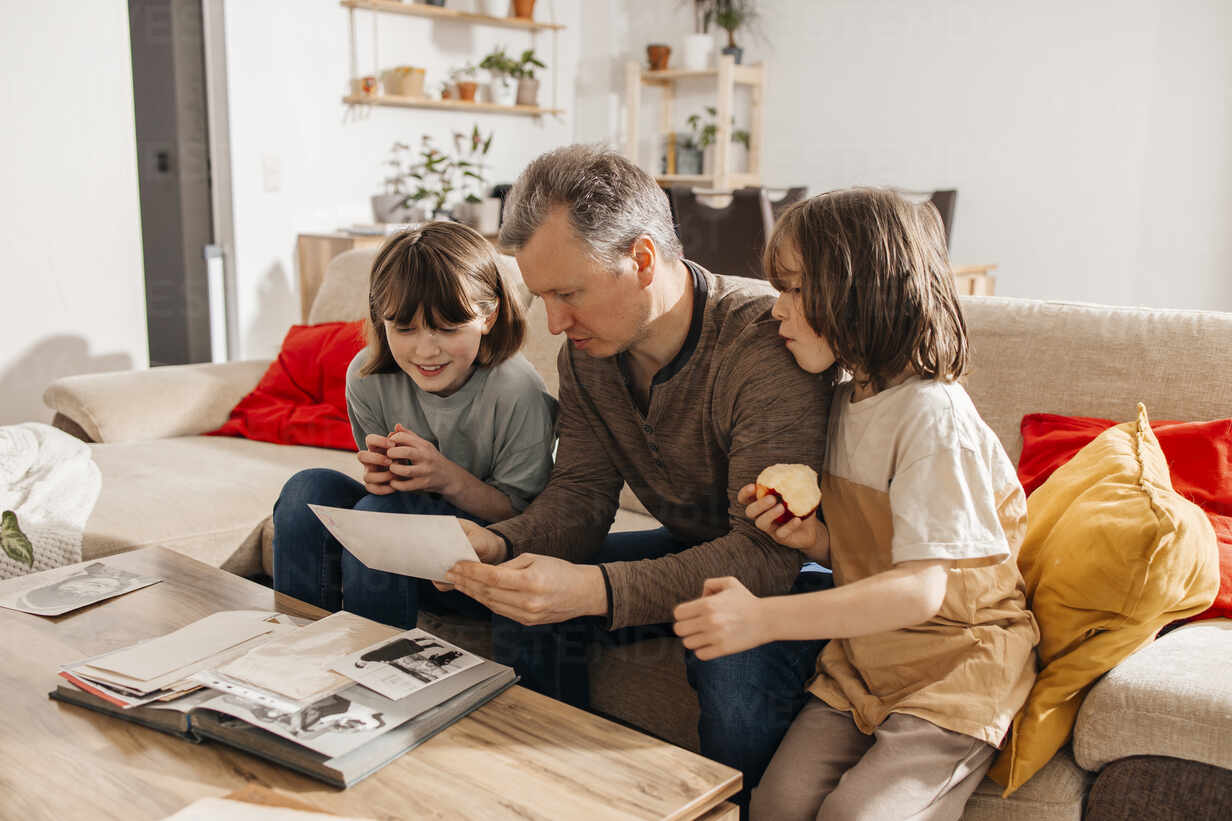 Father And Children Sitting On Sofa And Looking At Old Photographs In Living Room