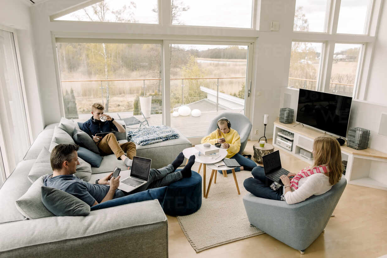 Familj Sitter I Vardagsrum Hemma Och Använder Teknik