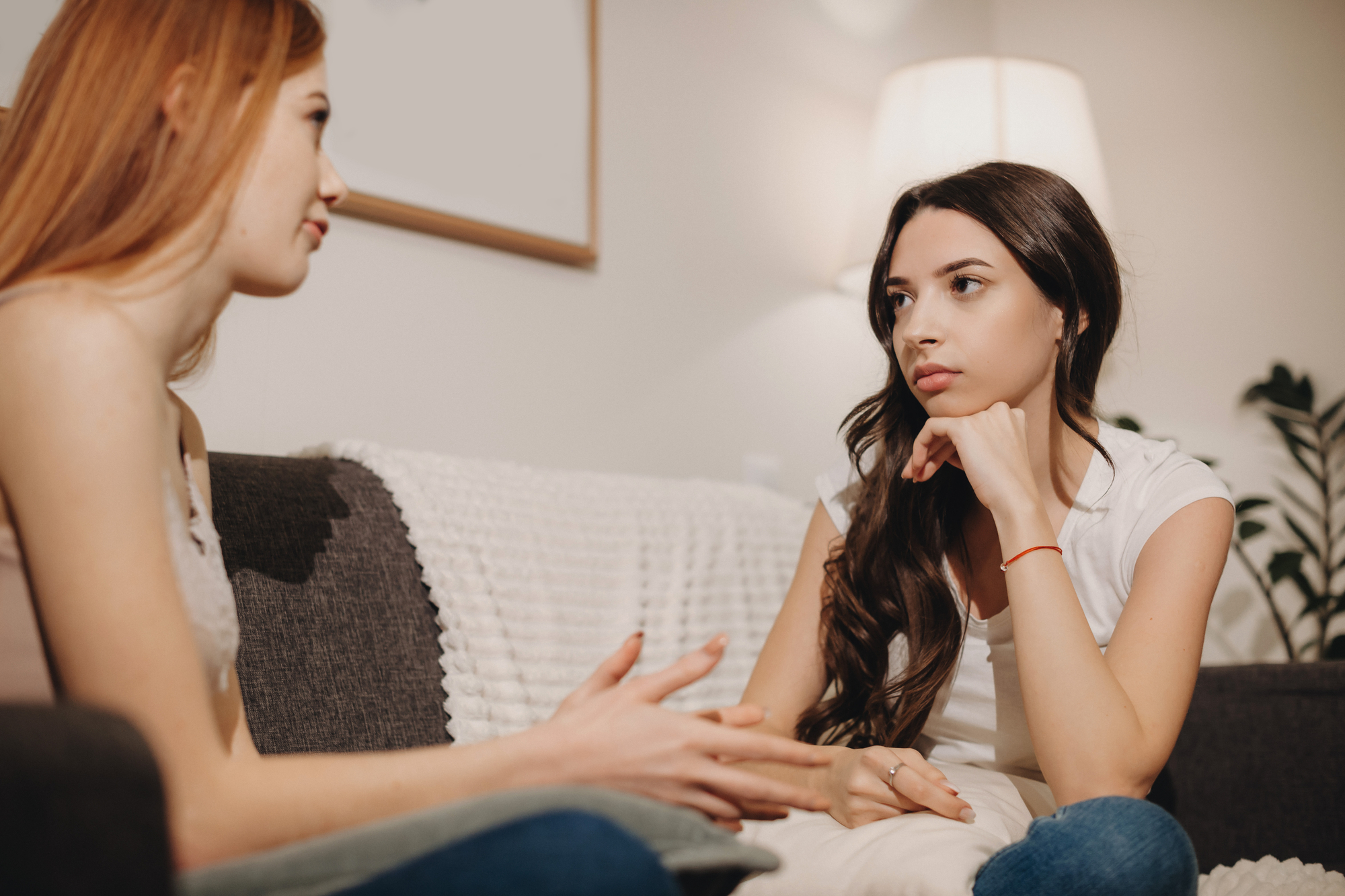 Lovely Red Haired Girl Is Explaining Something To Her Brunette Workmate During A Discussion On The Sofa